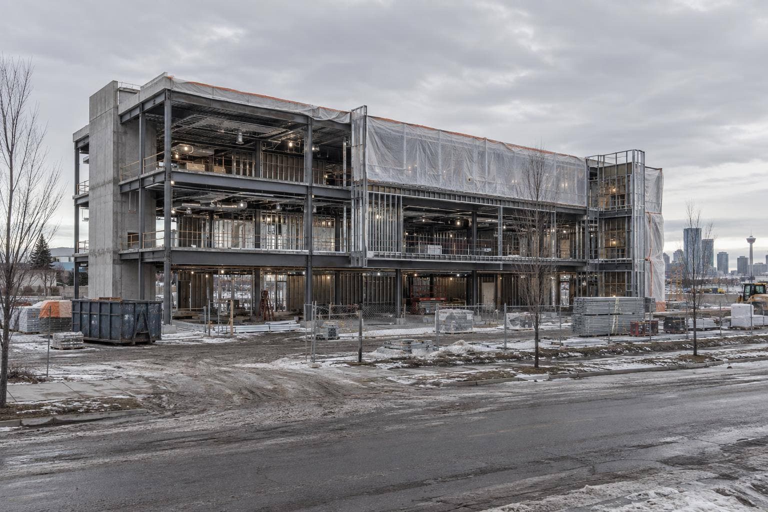 A commercial building under construction in Calgary, a gutted interior floor plate: steel stud framing, open ceiling with ductwork and conduit, layout marks on bare concrete, poly dust barriers.