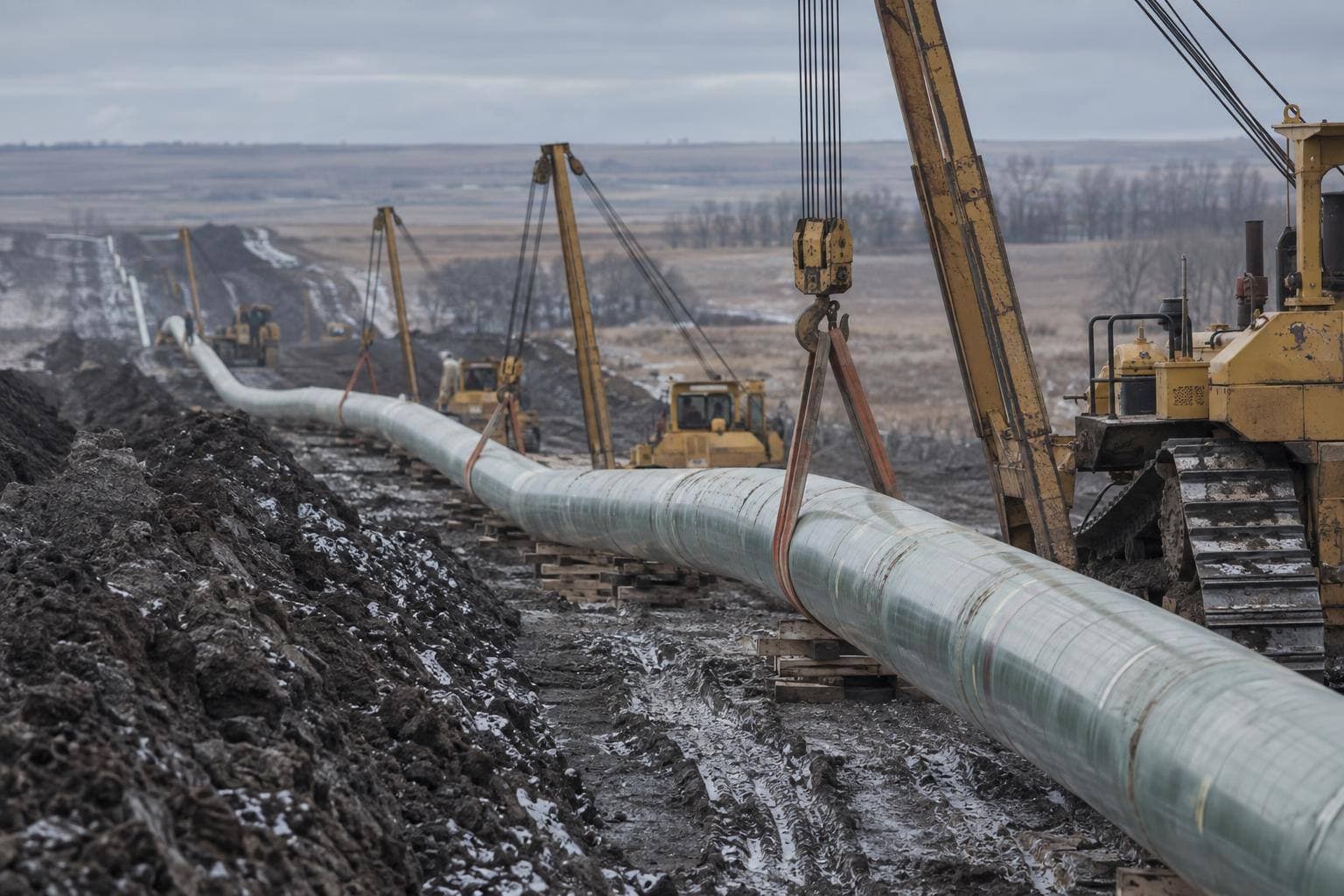 Welded pipe strung along a prairie right-of-way with heavy equipment beside it.