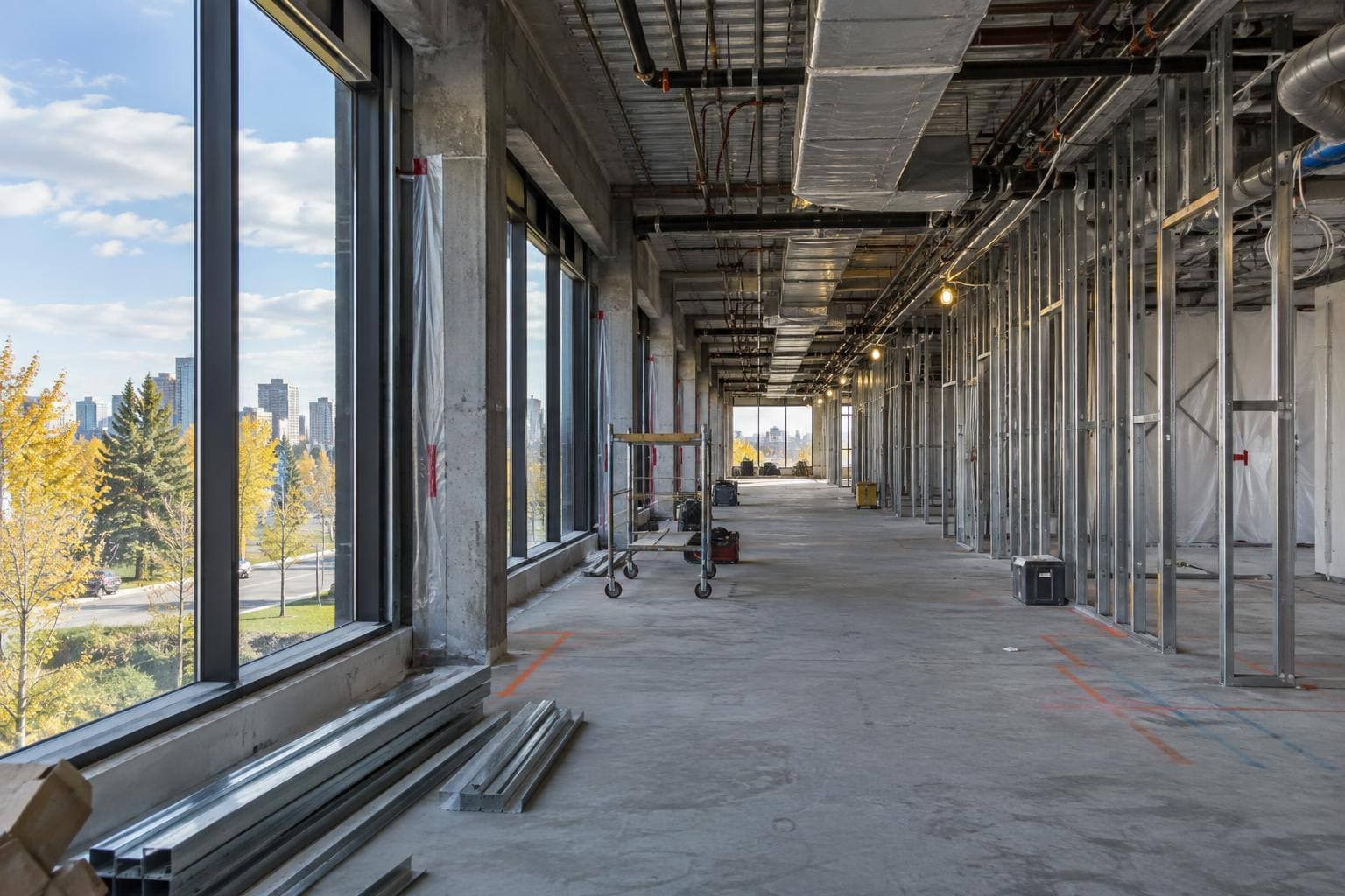 A gutted warehouse-office floor plate with steel studs, exposed ductwork and open service runs while trades prepare the interior for drywall and mechanical installation.