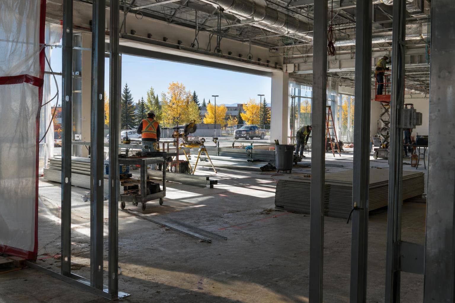 A stripped dealership interior with temporary partitions, exposed services and construction crews working across the floor plate, with no visible text or signage.