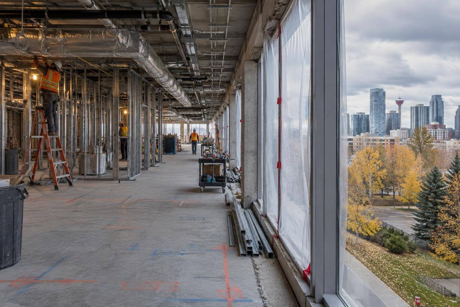 A gutted museum floor plate with temporary protection, exposed services, steel studs and crews installing mechanical and electrical systems inside the renovation area.