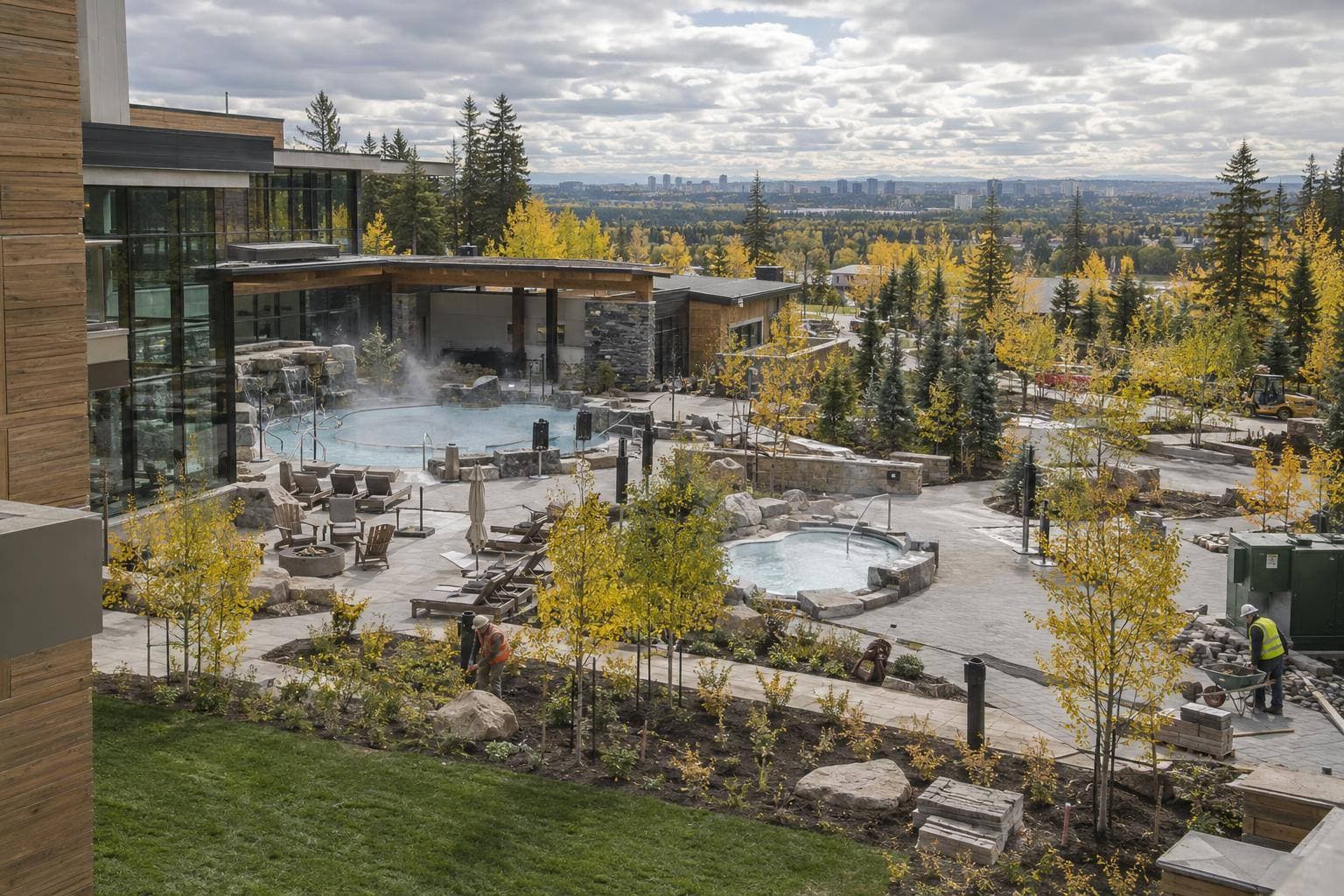 A documentary photograph of the completed thermal spa construction site with workers finishing exterior landscaping and service areas beside the resort complex, with no visible signage.