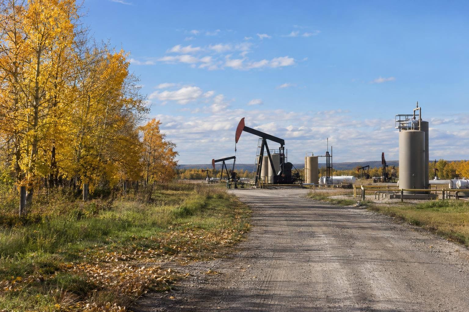 A documentary photograph of an Alberta oilfield with pumpjacks, storage tanks and service equipment operating under an open sky, with no logos or text visible.